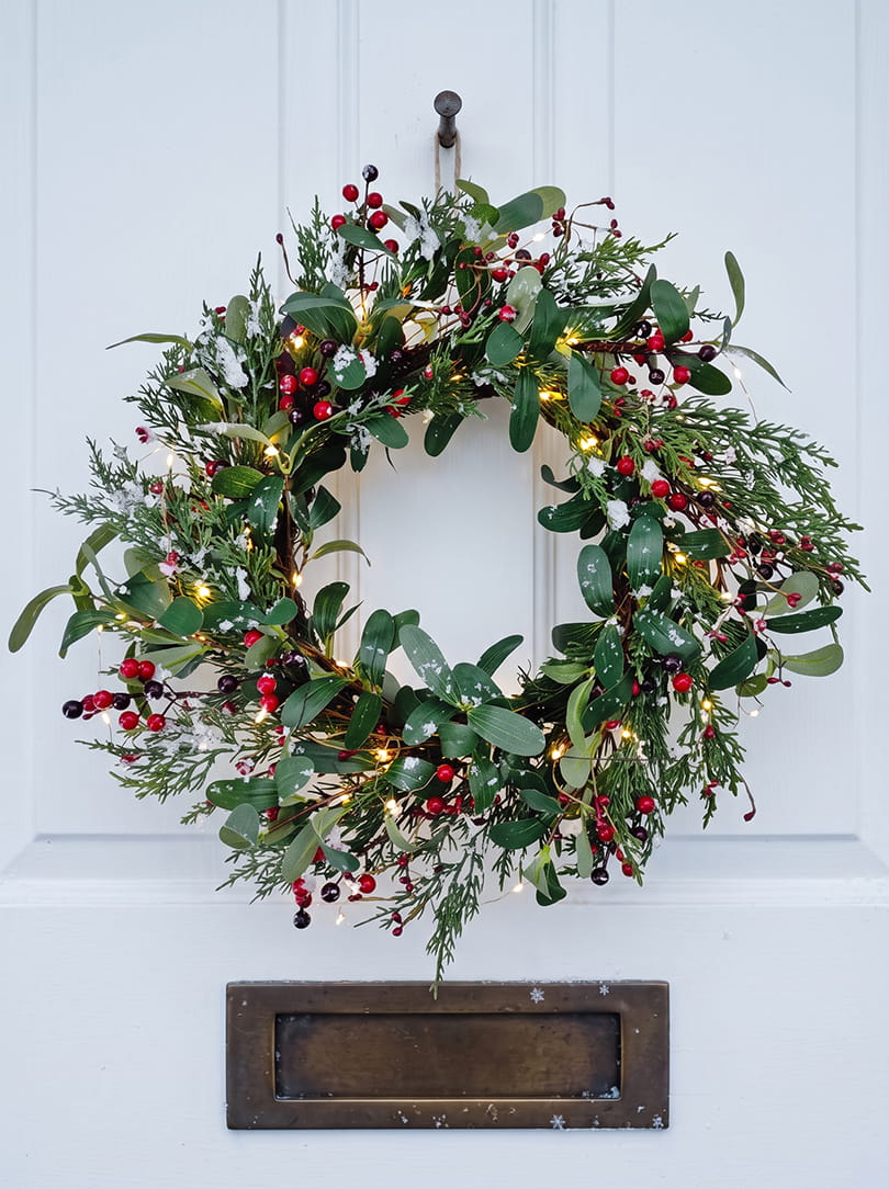Kerstkrans aan witte voordeur met lampjes